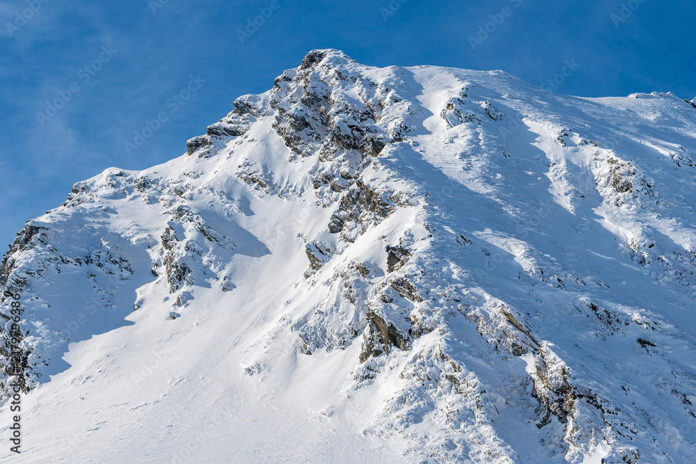 Fototapeta premium Dramatic snow-covered alpine ridge and rugged rock formations beneath clear blue winter sky in the Romanian Carpathians.