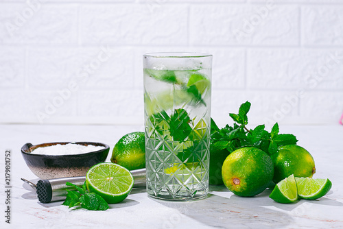 Fresh drink made with lime and mint sits on a table with limes and sugar nearby