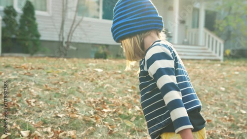 Boy walking across a leaf-scattered autumn lawn while holding a tricycle handle