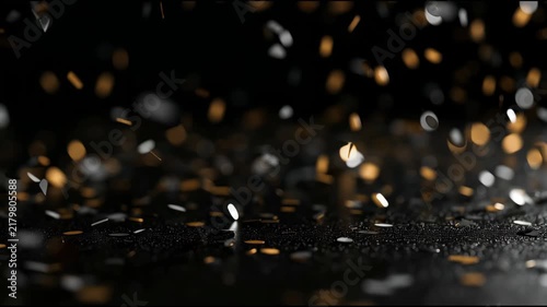 Golden confetti slowly swirls and falls through the air on a dark background, like shimmering stardust on a festive night. New Year and Christmas video for winter projects, intros and holiday ads.