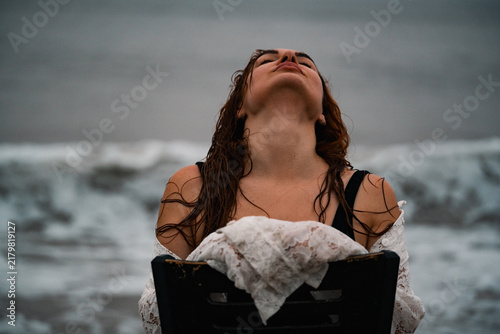 Canvastavla Woman sitting on a chair by the ocean with wet hair at the beach during sunset