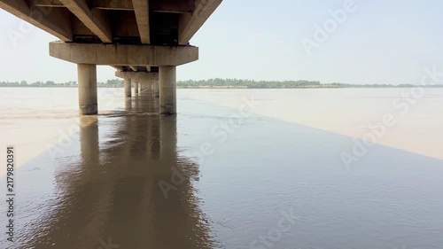 A close-up view of a vast river filled with flowing water and natural surface eddies, as it flows calmly beneath a sturdy bridge. 4k video