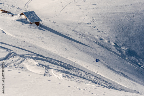 Fotografie Remote rustic shelter surrounded by untouched snow and long winter shadows in the Fagaras Mountains