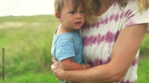Mother carrying her toddler while walking through a lush green field on a summer day