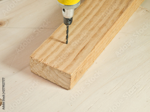 Bild auf Leinwand Drill Bit Penetrating Wooden Plank - A close-up view of a metal drill bit from a