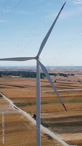 Renewable energy and sustainability, vertical video, close-up aerial drone shot flying to the right around a spinning wind turbine in a rural landscape