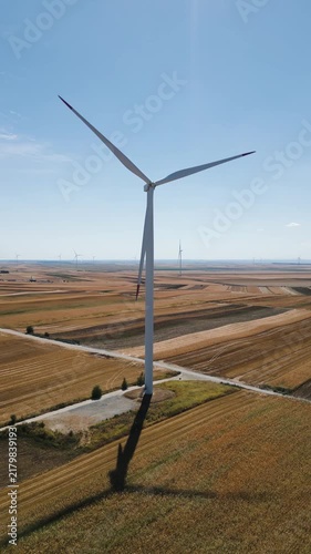 Renewable energy and sustainability concept, wind turbine generating electricity in a rural field, vertical aerial drone shot of clean power infrastructure