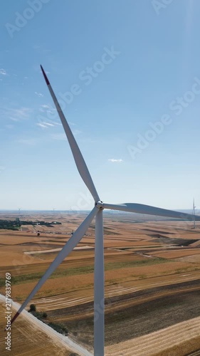 Renewable energy and sustainability concept, wind turbine blades rotating over agricultural fields, vertical aerial drone shot of clean power infrastructure