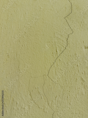 Cracked plaster texture – Pale yellow stucco wall background with fissures.