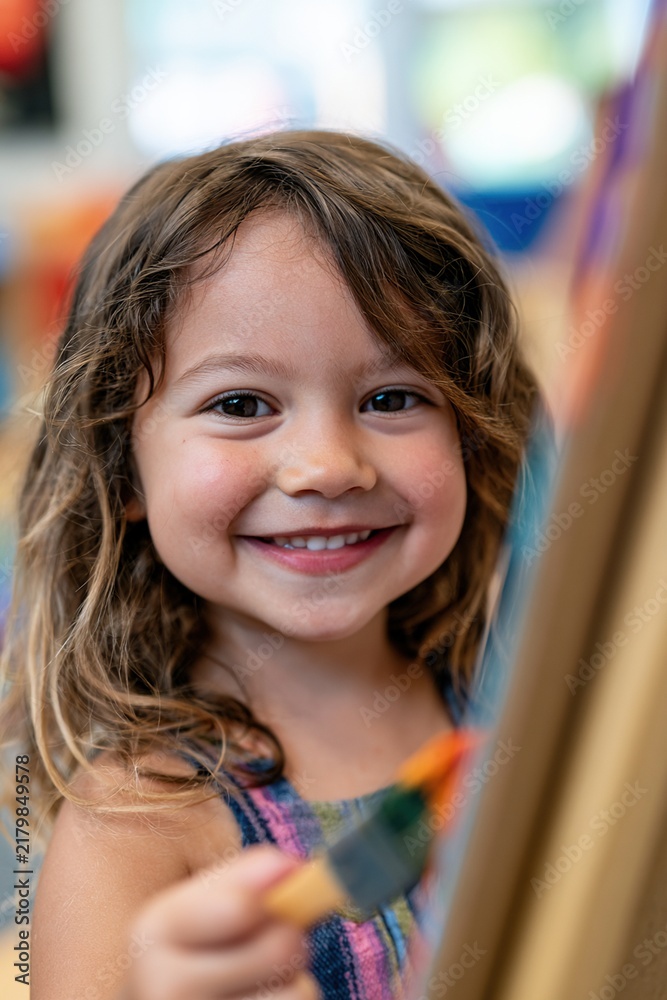 Fototapeta premium Preschool child smiling and offering paintbrush at shared easel