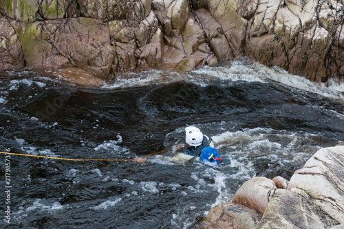 Person in protective gear training for a swift water rescue in a rocky powerful river. Extreme sports, adventure, people active outdoors