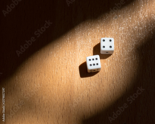 White dice resting on a wooden surface, partially illuminated by sunlight