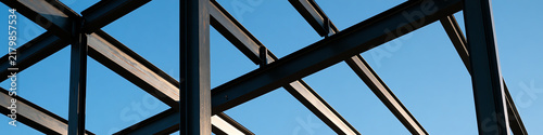 A close-up view of a metal framework against a clear blue sky, showcasing contemporary architectural design and construction methods, emphasizing structure.