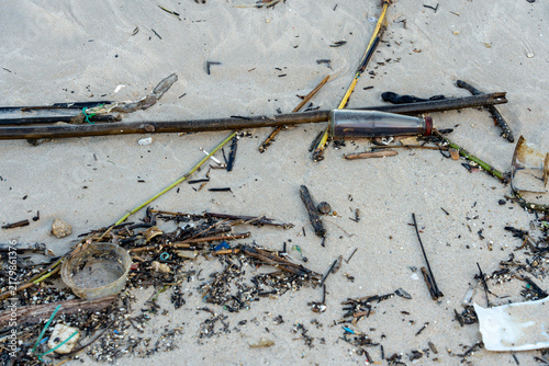 Foto A top-down view of environmental pollution on a sandy beach, featuring a discarded glass bottle, plastic fragments, and washed-up wooden debris