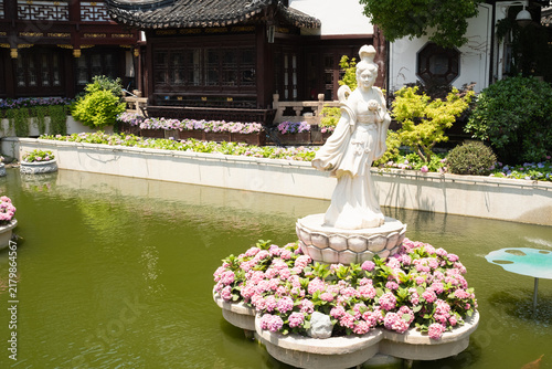 Photography Shanghai Yu Garden pond with white guardian statue on floral pedestal above gree