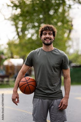 Konstfotografi Young man smiling holding basketball on outdoor court