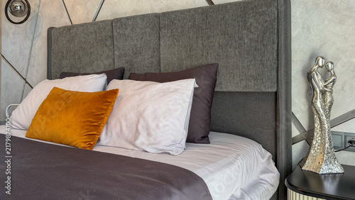 Stylish modern bedroom interior with upholstered bed, decorative pillows, mirrored wardrobe and contemporary geometric wall design.