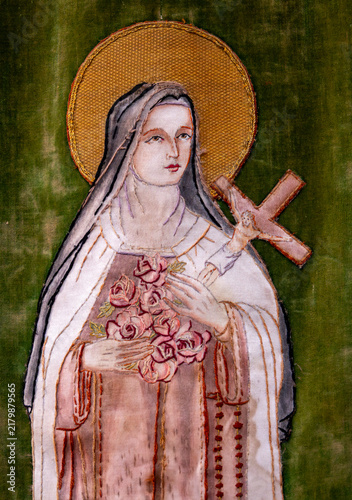 An embroidered religious textile depicts Saint Therese of Lisieux holding a crucifix and a bouquet of roses.
