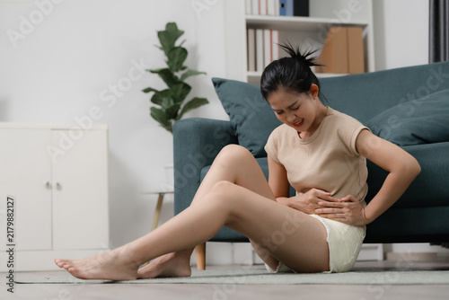 Canvastavla Menstrual cramps and period pain concept showing a woman holding her lower abdomen while sitting on the floor at home in discomfort
