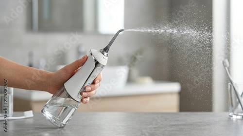 A hand holding a white electric spray bottle spraying water from the nozzle.