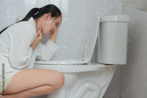 Cuadro en lienzo Nausea and vomiting concept showing a sick woman kneeling beside a toilet in a bathroom, holding her throat and head in discomfort