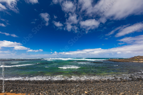Panoramic view of a volcanic beach and the turquoise Atlantic Ocean under a blue sky on Fuerteventura (Canary Islands) – a background or wallpaper for your project