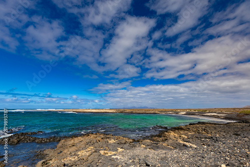 Panoramic view of a volcanic beach and the turquoise Atlantic Ocean under a blue sky on Fuerteventura (Canary Islands) – a background or wallpaper for your project