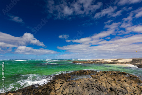 Panoramic view of a volcanic beach and the turquoise Atlantic Ocean under a blue sky on Fuerteventura (Canary Islands) – a background or wallpaper for your project