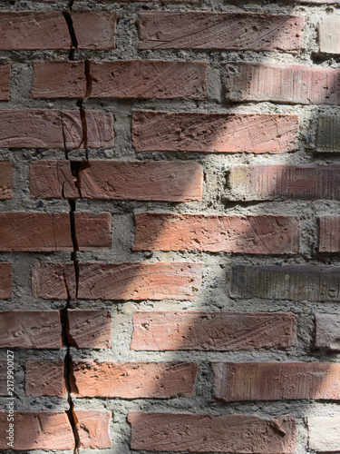 Sunlight on a red brick wall texture cracked by structural damage and vertical fissures