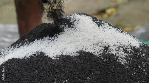 Dark Organic Fertilizer Powder Pouring onto White Chemical Granules Heap Close Up. Pouring Dark Soil Mineral Additive onto White Chemical Fertilizer Granules Heap.