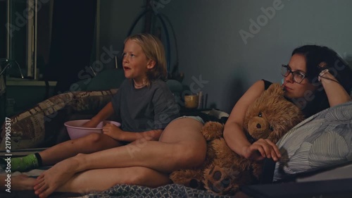 Young mother and her son relaxing on the sofa, watching a movie and eating popcorn in the evening