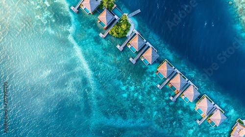 Aerial view of overwater bungalows, turquoise ocean, a small island, and deep blue channels