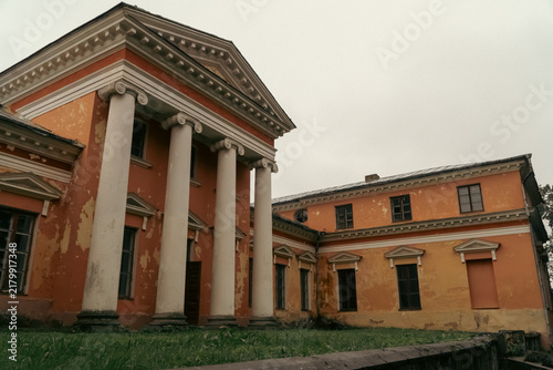 Fotografie A wide angle view captures the weathered yellow-orange facade and Ionic columns of an old neoclassical estate building against an overcast sky
