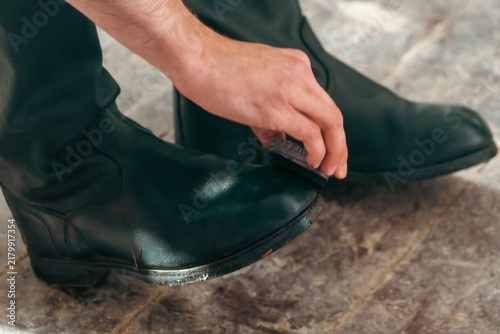 Canvastavla A close-up view shows a man cleaning and polishing his black leather boots using a small brush