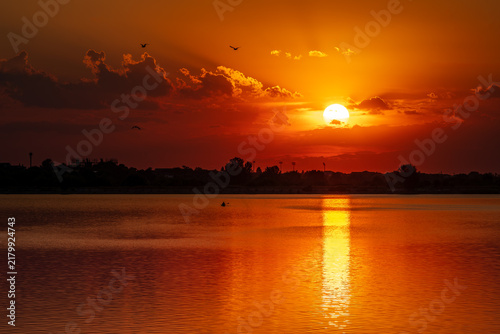 Dramatic orange sunset over Lacul Morii lake in Bucharest with kayakers silhouette.