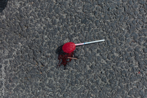 Obraz na plátně A discarded red lollipop melting into black asphalt in the summer heat, leaving a sticky red pool and wooden splinters