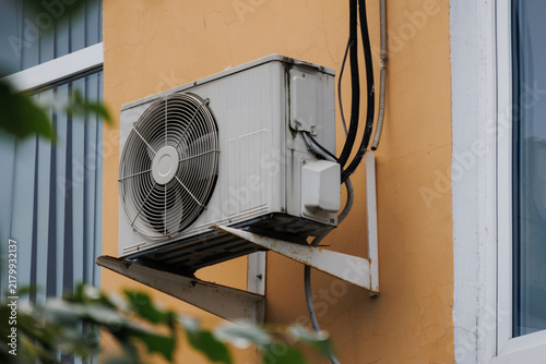 White AC unit mounted on yellow wall with green leaves. High quality photo.