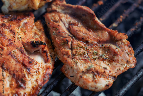 Pork and chicken steaks grilling on charcoal barbecue with open flames during outdoor cooking and summer barbecue