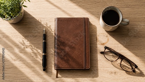 Overhead flat lay of a leather notebook pen mug and glasses