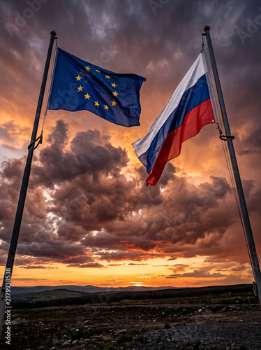 flags of the european union and russia waving on flagpoles against sunset sky and dramatic clouds international politics