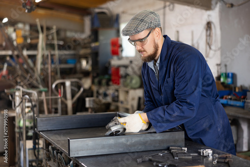 Experienced mechanic uses an angle grinder while working at a machine-building plant