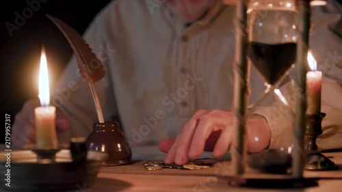 man prodding through a pile of coins then writing on paper with a quill pen