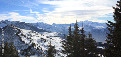 Panoramic winter view of snow covered mountains framed by evergreen trees and dramatic lenticular clouds near Morzine Avoriaz in the French Alps, France.