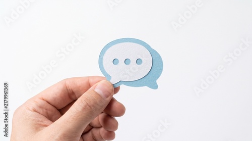 Hand holding a blue and white paper speech bubble with three dots representing conversation or thinking