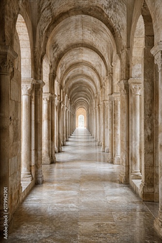 Ancient stone corridor with rows of arches and columns in old monastery. Symmetry and perspective of medieval roman architecture.