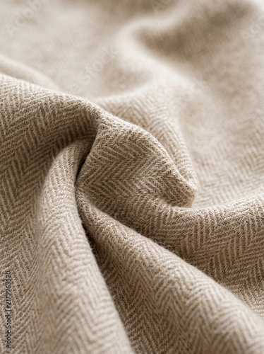 Close-up of beige fabric with a herringbone weave, showing soft folds and texture, symbolizing natural warmth, comfort, and textile design