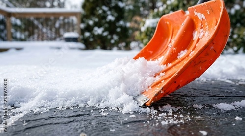 Orange snow shovel clearing thick white powder from dark stone patio, winter home maintenance labor, manual snow removal task, seasonal outdoor chores.