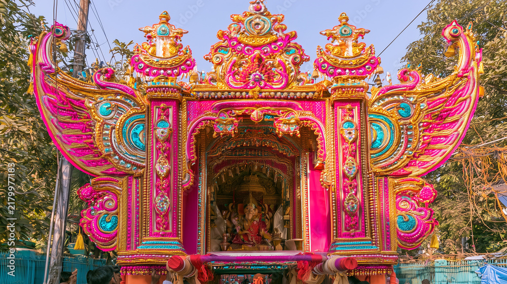 Fototapeta premium Front view of an elaborate Hindu Antyesti ceremonial structure decorated with vivid pink, gold and turquoise ornaments, intricate handcrafted patterns, wing-shaped details and a sa