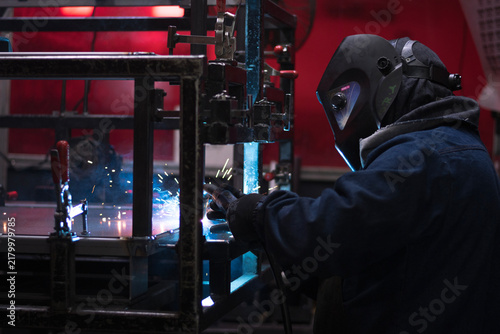 Принти на полотні Professional welder wearing protective helmet fabricating steel frame with spark
