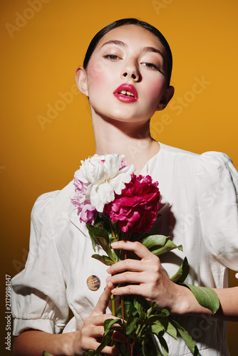Foto Fashion model with glossy makeup poses holding red and white flowers